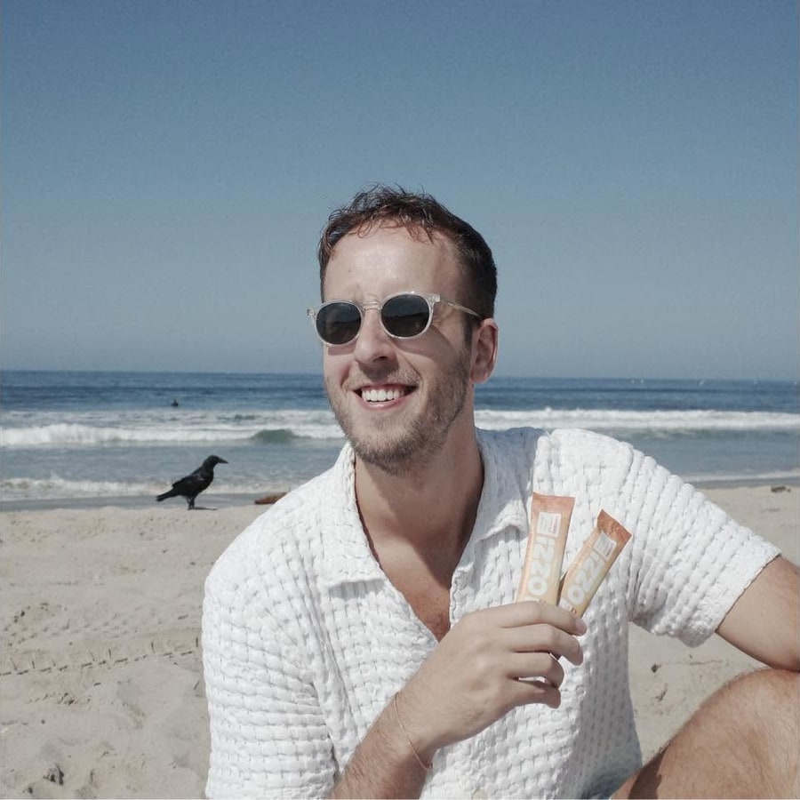 Brandon Kuipers on the beach, holding two Ozzi drink sticks